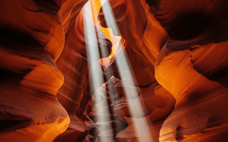 Narrow slot canyon with sunbeams streaming through sandstone walls, glowing orange textures