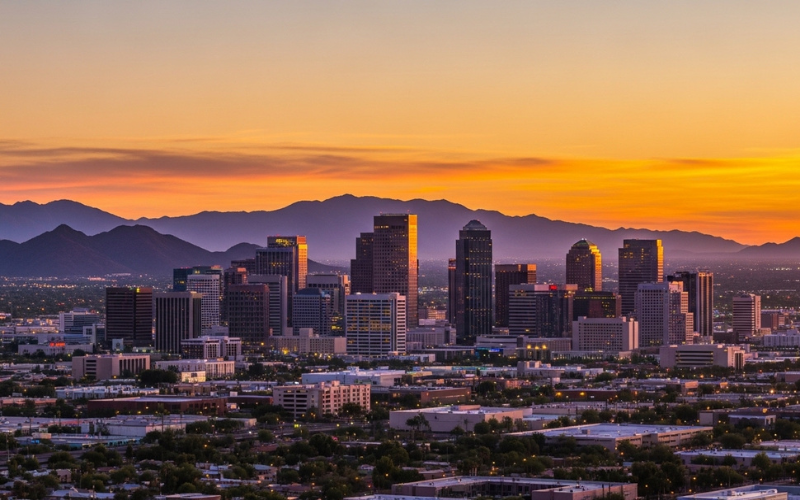Phoenix skyline at sunset with desert mountains behind city, warm glowing sky